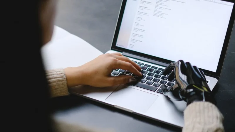 Iemand met een handprothese bedient een laptop